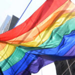 BULLS AXE Rising Star Over Pride Month Rant A vibrant rainbow flag waving against a city backdrop