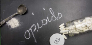 Spoon, syringe, and pills on a black surface with the word 'opioids' written in chalk