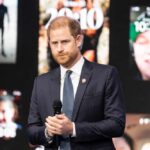 ROYAL Identity: Is Harry Using It For Cash? A man in a suit speaking at a conference with digital screens in the background