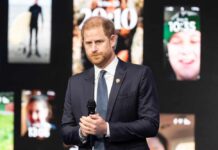 A man in a suit speaking at a conference with digital screens in the background