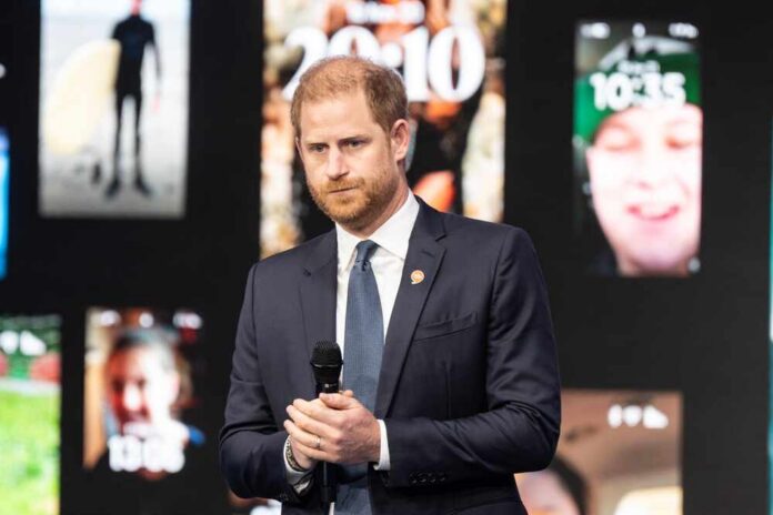 A man in a suit speaking at a conference with digital screens in the background