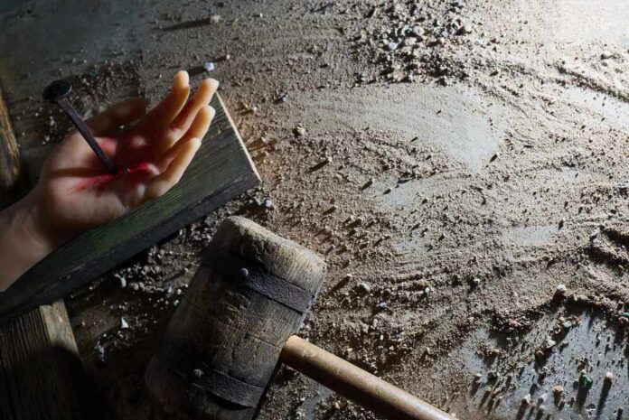 shutterstock_2759557775.jpg An artificial hand with a nail embedded and blood effects on a textured surface