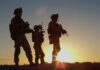 Silhouetted soldiers standing against a sunset
