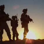 Silhouetted soldiers standing against a sunset