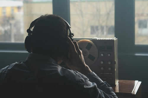 espionage-2164991019 Person listening to audio reel beside window