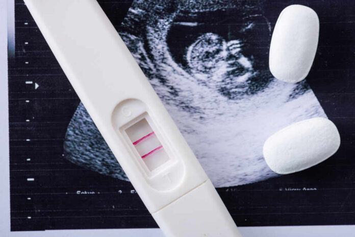 shutterstock_1506812507.jpg Pregnancy test next to an ultrasound image and two white pills