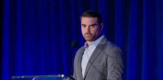 A man in a gray suit speaking at a podium during a conference
