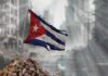 Invasion Chatter Spikes — Proof Still Missing Worn Cuban flag standing on rubble in a desolate urban environment