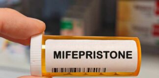 A hand holding a prescription bottle labeled Mifepristone