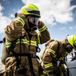 Firefighters in protective gear standing outside cloudy sky