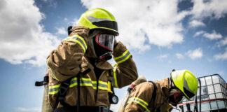 Firefighters in protective gear standing outside cloudy sky