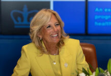 Jill Biden Link, No Details — What’s Missing? Smiling woman in a yellow blazer at a meeting table