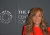 Woman with wavy hair in a bright red dress at media event backdrop