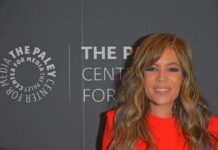 Woman with wavy hair in a bright red dress at media event backdrop