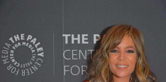 Woman with wavy hair in a bright red dress at media event backdrop
