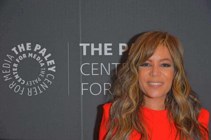 Woman with wavy hair in a bright red dress at media event backdrop