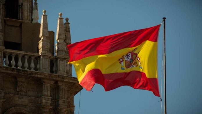Spanish,Flag,Waving,In,Front,Of,A,Cathedral Spanish flag waving against a clear blue sky