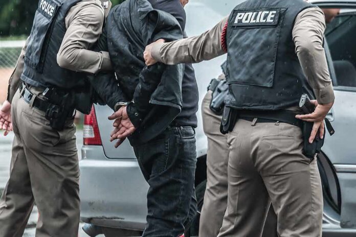Police officers arresting a person beside a car
