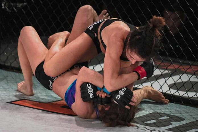 two female mixed martial artists grappling on the mat in a cage
