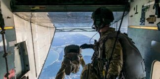 Paratroopers jump from a military aircraft over coastline