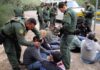 Law enforcement officers process a seated group outdoors
