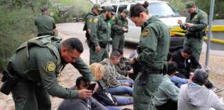 Law enforcement officers process a seated group outdoors