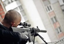 Person aiming a scoped rifle from a balcony